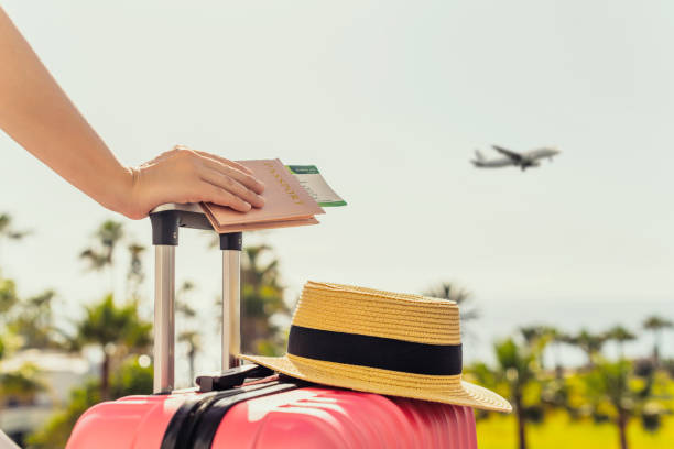 istockphoto-1392494719-612x612 Woman with pink suitcase and passport with boarding pass standing on passengers ladder of airplane opposite sea with palm trees. Tourism concept