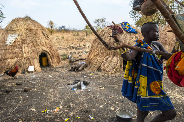 OMORATE, ETHIOPIA - JANUARY 24: Unidentified woman from Mursi tribe posing for a portrait next to a tree with the traditional houses of the Mursi in the background on January 24, 2018 in Ethiopia.