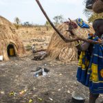 OMORATE, ETHIOPIA - JANUARY 24: Unidentified woman from Mursi tribe posing for a portrait next to a tree with the traditional houses of the Mursi in the background on January 24, 2018 in Ethiopia.